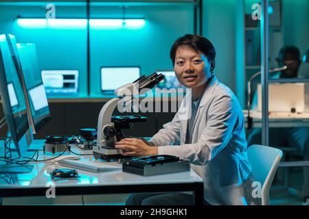 Young successful chinese female researcher with microscope looking at camera by workplace in laboratory Stock Photo
