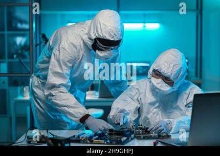 Two contemporary lab workers in protective coveralls consulting about repairment of motherboard or microprocessor Stock Photo