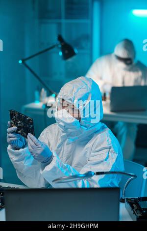 Young female in protective coveralls holding motherboard while checking it before repairing Stock Photo