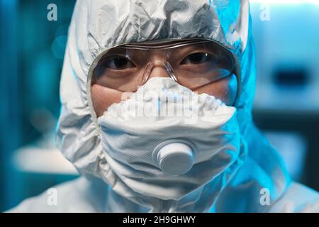Face of young Asian female scientist in protective respirator, eyeglasses and coveralls Stock Photo