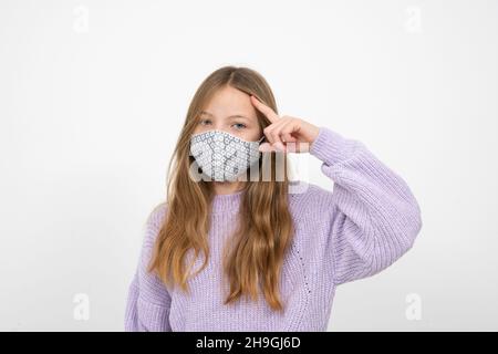 pretty blonde girl in purple wool sweater with nose mouth mask is standing in front of white background Stock Photo