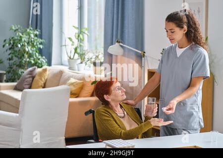 Elderly woman using wheelchair taking medicine giving by the nurse during her disease Stock Photo