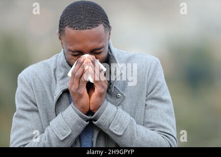Ill man with black skin blowing on tissue outddors in winter