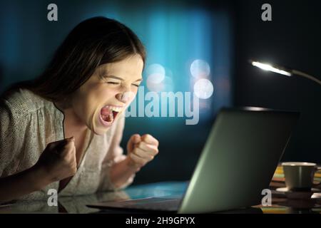 Excited woman checking laptop news at home in the night Stock Photo