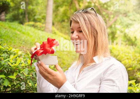 girl opens a gift. woman in white shirt holding a gift box with a red bow Stock Photo