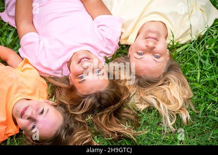 Happy loving family is resting in the park.  Mom and 2 daughters laugh.  Woman and children girls lie on their backs on the grass Stock Photo