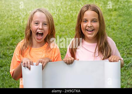 happy children with a white billboard for advertising on a background of grass. Stock Photo
