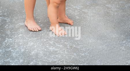 Child and baby feet on the asphalt. The child helps the youngest to take the first steps. Stock Photo