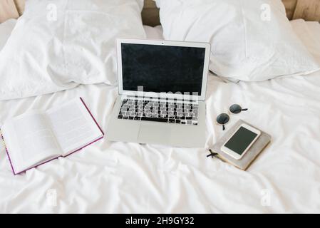 Photo of young joyful woman in pajama typing on laptop and smiling while sitting on bed in light room Stock Photo