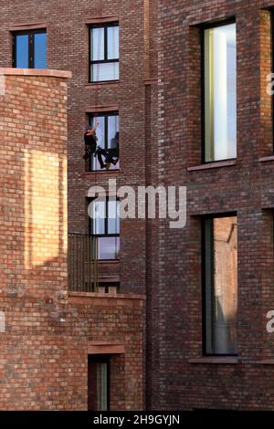 Window cleaner at work (abseiler signalling, new high-rise apartments building, safety) - Hudson Quarter York city centre, North Yorkshire England UK. Stock Photo