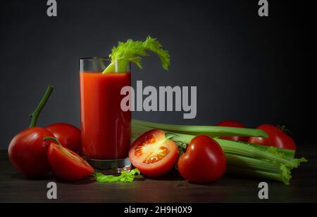 Tomato juice with tomatoes and celery sticks on a dark background. Stock Photo