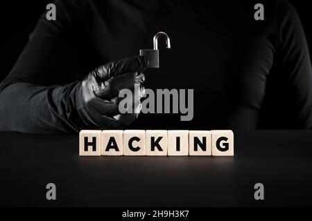 Hacking and hacker concept. The word hacking on wooden blocks with a hacker holding an open padlock background. Stock Photo