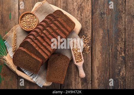Rye bread cut into pieces and wheat seeds on a wooden background. Top view, copy space. Stock Photo