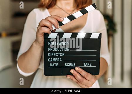 A woman in her hA woman in her hands holds a black board with a clapperboard while shooting a film, video. Cinema tablet in video production. Take, st Stock Photo