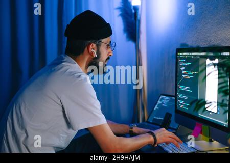 Young man mobile developer writes program code on a computer, programmer work in home office. Stock Photo