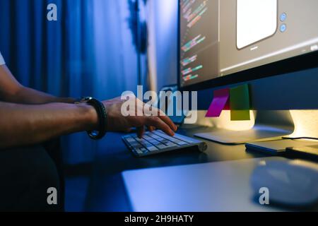 Mobile developer writes program code on a computer, typing on keyboard, programmer work in home office. Stock Photo