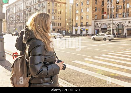 Portrait of a young woman in a protective medical mask on her face on a city street. Pandemic coronavirus. Stock Photo