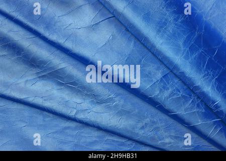 Draped crumpled silk of cobalt blue color background. Texture of folded coral blue shiny silk cloth. Design element of elegant luxury silky fabric. Stock Photo