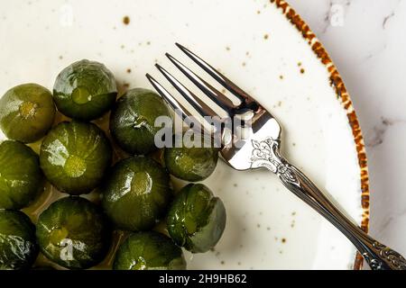 Top view of preserved whole green figs and dessert fork on a white porcelain plate. Sweet jam of unripe figs in syrup. Traditional mediterranean jam. Stock Photo