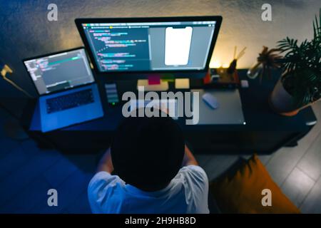 Young man mobile developer writes program code on a computer, programmer work in home office. Stock Photo