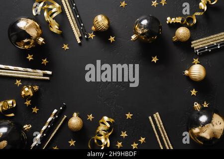 Composition with shiny luxury gold balls, drinking straws on black background with copy space. View from above. Greeting card or invitation for New Ye Stock Photo