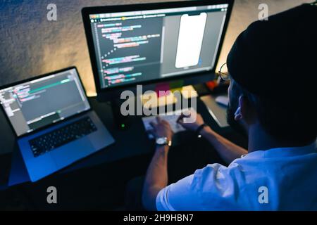 Young man mobile developer writes program code on a computer, programmer work in home office. Stock Photo