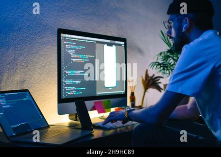 Young man mobile developer writes program code on a computer, programmer work in home office. Stock Photo