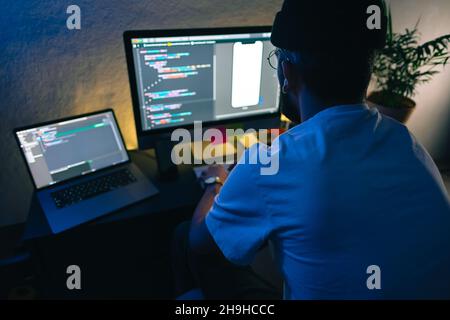 Young man mobile developer writes program code on a computer, programmer work in home office. Stock Photo