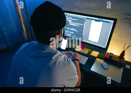 Young man mobile developer writes program code on a computer, programmer work in home office. Stock Photo