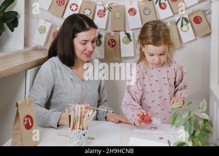 Mother with toddler child writing Christmas letter and doing advent calendar tasks in kids room. Festive activities for children at home. Happy Stock Photo