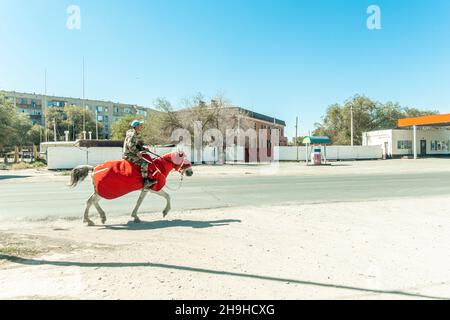 A man on a horse, animal dressed in red is riding on side of the road in Kyzylorda, Kazakhstan Stock Photo