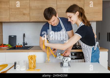 Young couple in aprons making pasta with noodle cutter. Family cooking vegan food at home. Concept of domestic lifestyle, healthy eating, happy marria Stock Photo