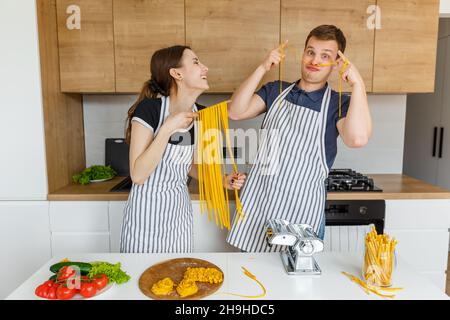 Young couple in aprons having fun with pasta noodles. Family cooking italian vegan food at home. Concept of domestic lifestyle, healthy eating, happy Stock Photo