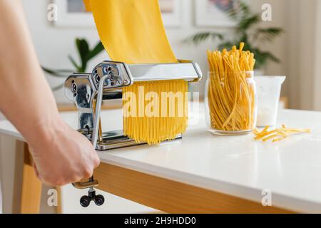 Man in apron making spaghetti with noodle cutter. Close-up pasta cooking at home. Preparing food from bright yellow dough. Stock Photo