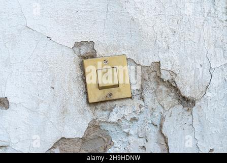 Plastic light switch on a wall with disintegrated plastering showing layers of сement Stock Photo