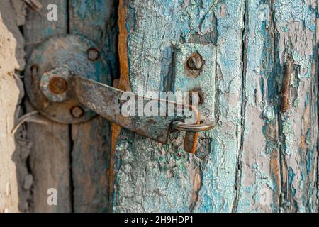 A rusty metal latch, with paint peeled, snapped shut on an old wooden door with paint weathered Stock Photo