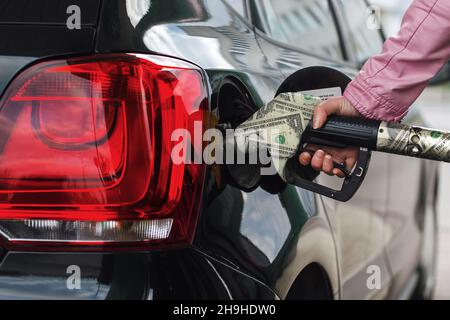 Woman's hand fuels the car. Girl at the gas station fills the tank with gasoline fuel. The rise in fuel prices, a concept idea. Filling gun and money Stock Photo