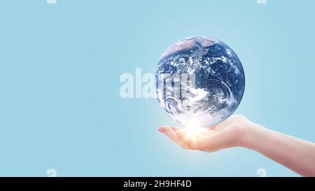 Hand holds blue planet Earth with sunset light on pastel blue color. Save Earth concept. Environment creative idea Stock Photo