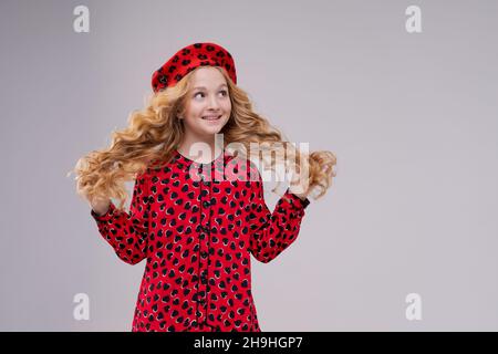 French fashion icon. Happy child wearing french red beret and dress on a light background. French little girl look. Little kid in french style. Fashionable style. All you need is surrender. Stock Photo