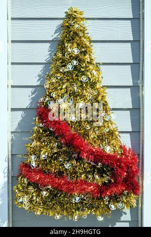 Decorated Christmas tree made by glossy gold and red paper on white wooden wall. Ornamental Christmas tree from stencil paper mounted on white wall du Stock Photo