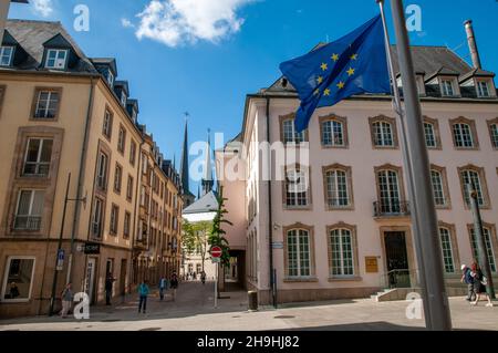 The EU flag waving by the Chamber of Deputies on Rue du Marché-aux-Herbes in Luxembourg city with the spires of Notre-Dame cathedral in the distance. Stock Photo