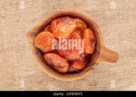Several sweet dry apricots in a wooden cup, close-up on burlap, top view. Stock Photo