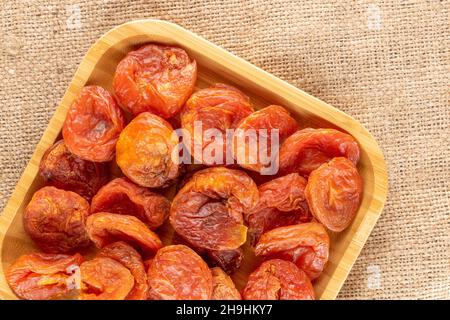 Several sweet dry apricots on a bamboo plate, close-up on burlap, top view. Stock Photo