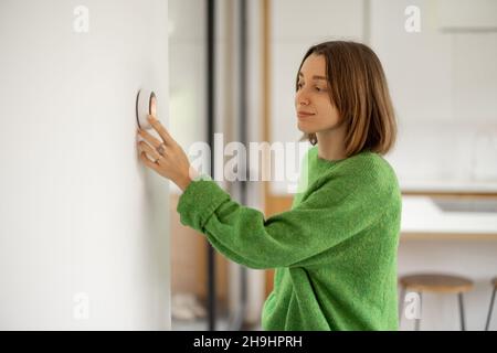 Woman controlling temperature with a smart thermostat at modern apartment. Stock Photo