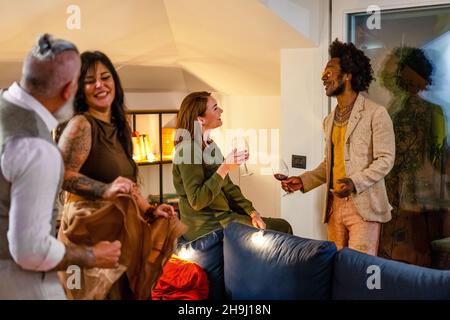 Diverse group of friends having fun, dancing and socializing. Adult people tasting red wine and smiling during a private house party, multiracial eleg Stock Photo