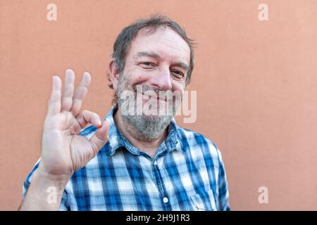 portrait of an old man showing okey symbol, expressing agreement, elder man wearing blue plaid shirt, pink color background, copy space Stock Photo
