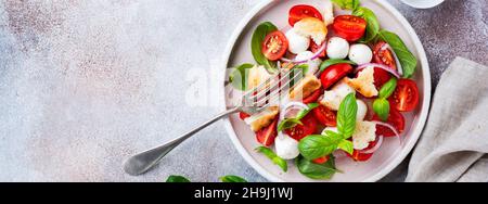 Traditional Italian salad Panzanella with cherry tomatoes, mozzarella cheese, basil and bread in ceramic plate. Top view. Stock Photo