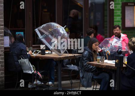 People dine at tables with umbrellas outside a restaurant in central London. Stock Photo