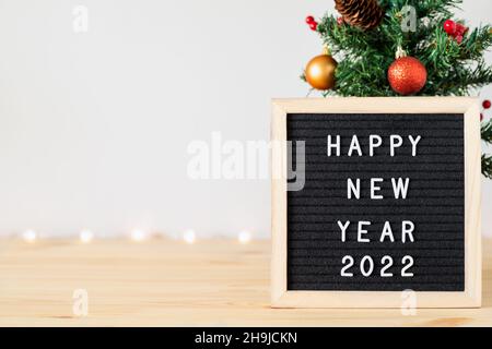 Happy new year 2022 text on felt letter board and Christmas tree with holiday decorations on table. Copy space on one side for text