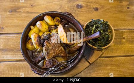 Roasted goatling or roasted kid "cabrito assado" ready to eat on a wooden table. Served with roasted potatoes and sprouts. Typical portuguese dish Stock Photo